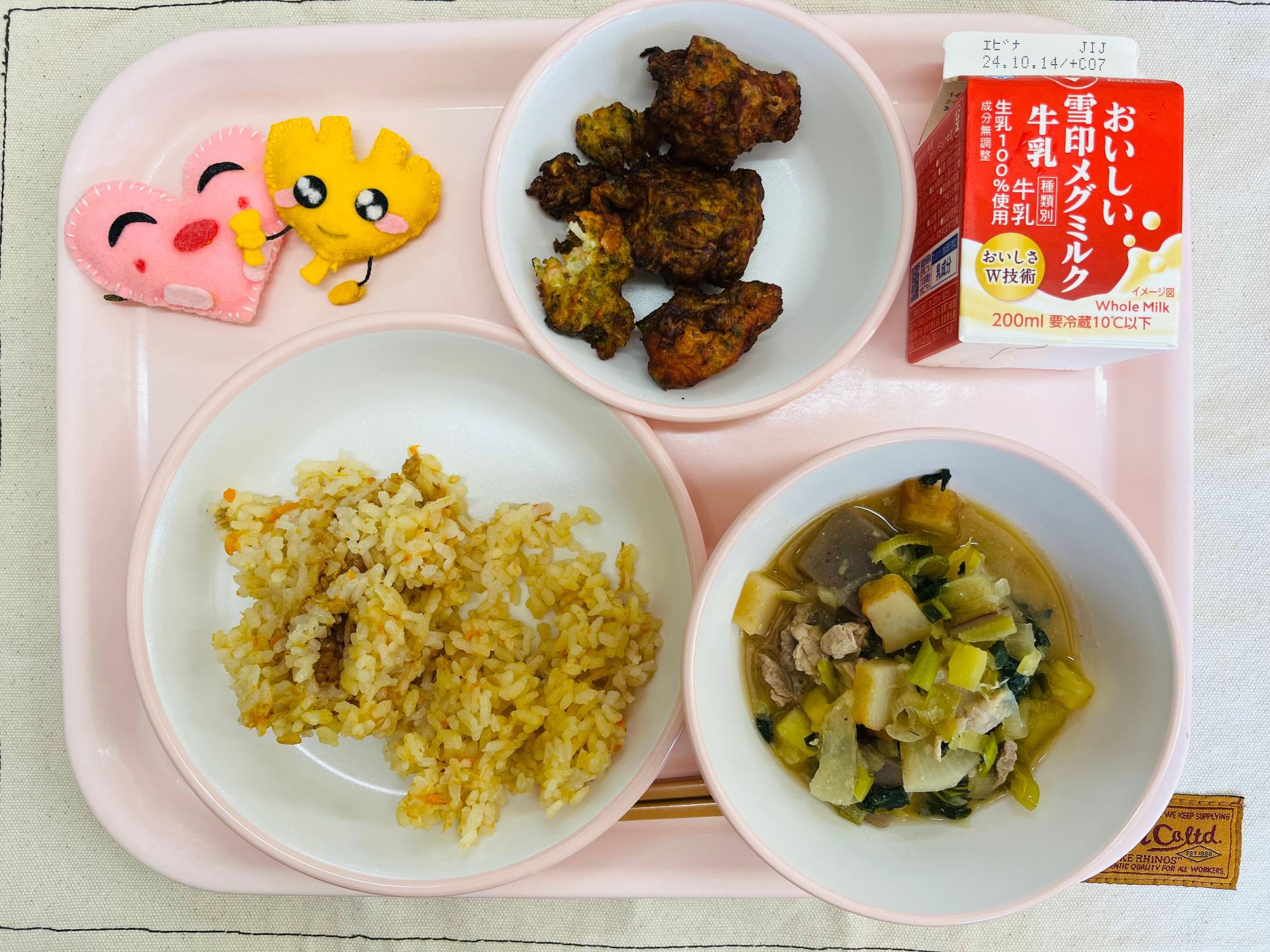 ピンクのトレーに給食が右上から反時計回りで牛乳、鮭のふうみあげ、ハートの形をした黄色とピンク色の布製マスコット、ゆうやけごはん、さつま汁と並べられている写真