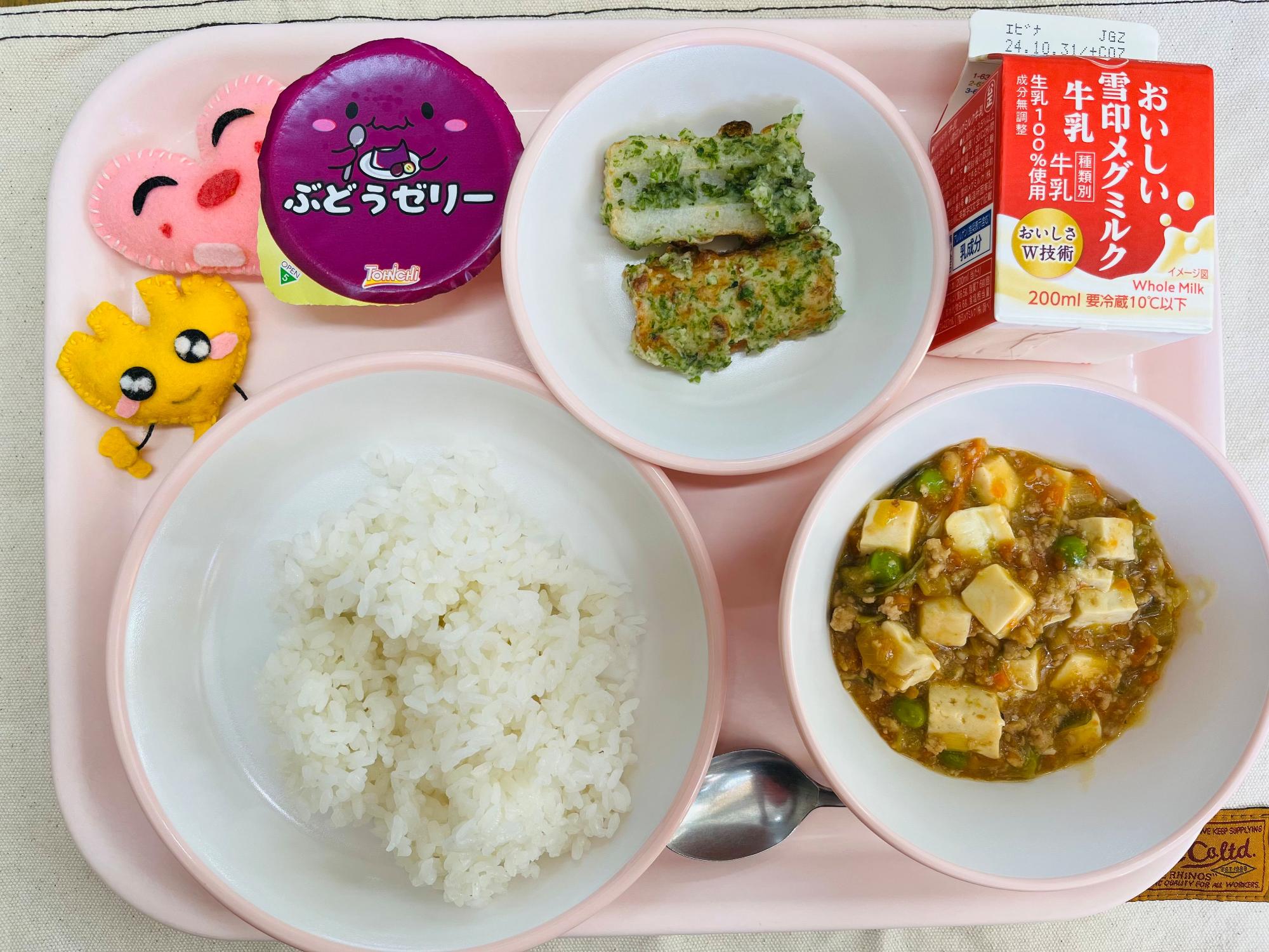 ピンクのトレーに給食が右上から反時計回りで牛乳、ちくわの磯部揚げ、ぶどうゼリー、ハートの形をした黄色とピンク色の布製マスコット、ごはん、マーボー豆腐と並べられている写真