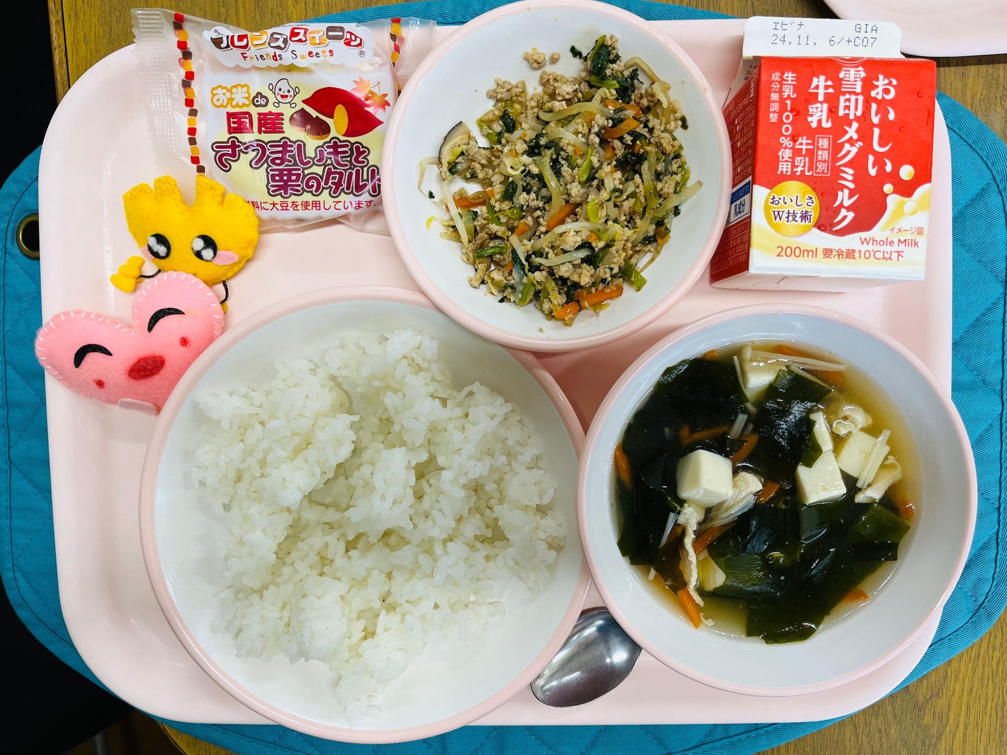 ピンクのトレーに給食が右上から反時計回りで牛乳、ビビンバの具、サツマイモと栗のタルト、ハートの形をした黄色とピンク色の布製マスコット、ごはん、わかめスープと並べられている写真