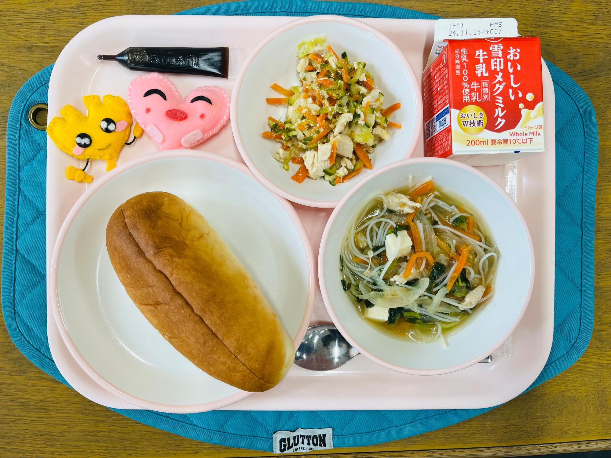 ピンクのトレーに給食が右上から反時計回りで牛乳、バインミー、ミルメーク、ハートの形をした黄色とピンク色の布製マスコット、パン、ビーフンスープと並べられている写真