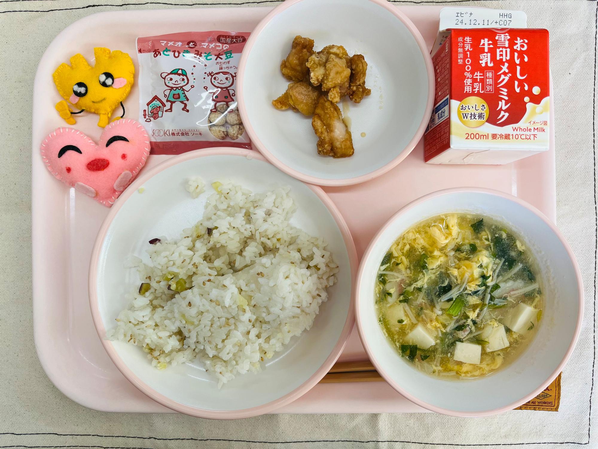 ピンクのトレーに給食が右上から反時計回りで牛乳、チキン南蛮、みそだいず、ハートの形をした黄色とピンク色の布製マスコット、サツマイモごはん、かきたま汁と並べられている写真