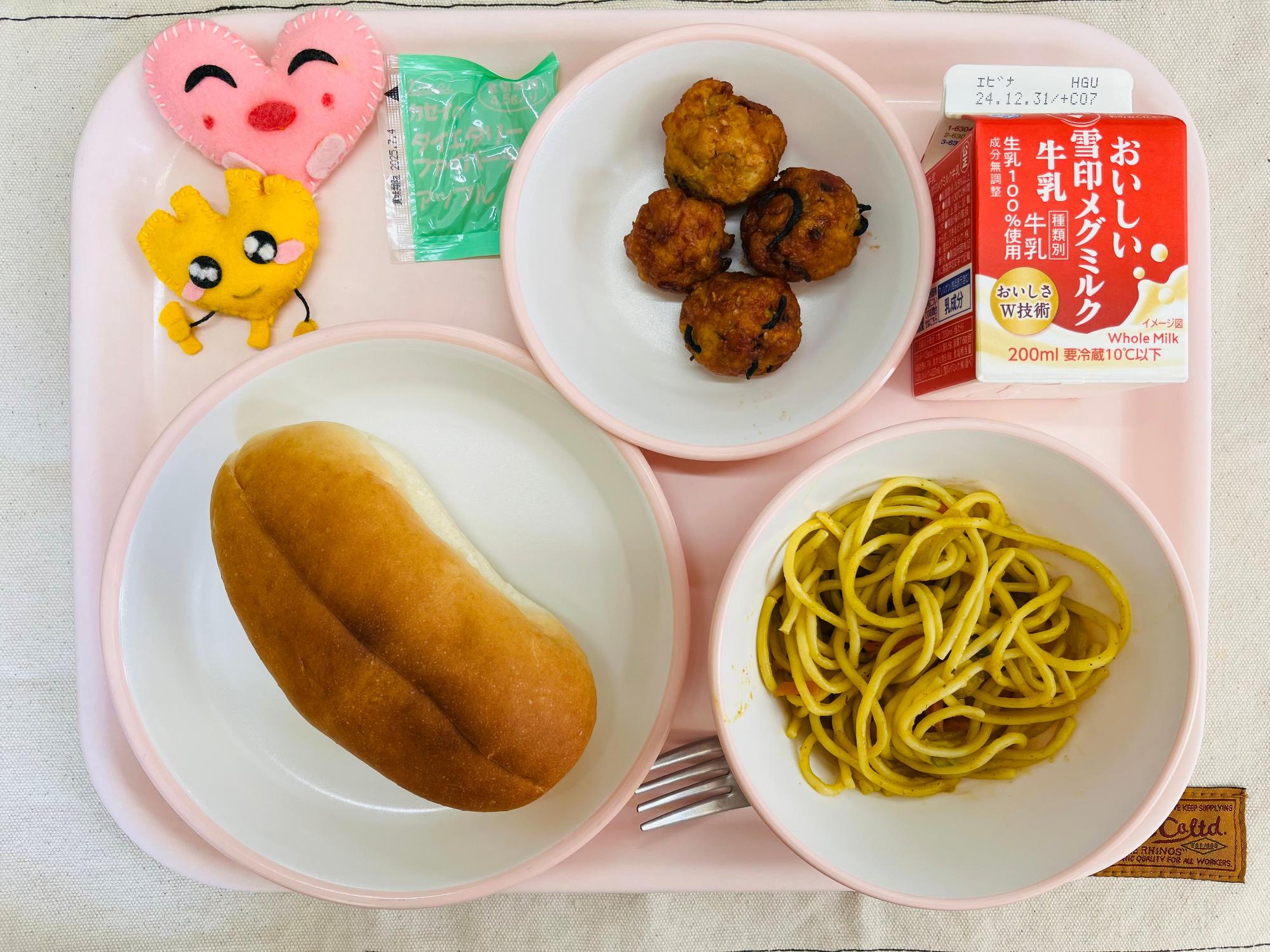 ピンクのトレーに給食が右上から反時計回りで牛乳、豆腐ボールのケチャップソースあえ、りんごジャム、ハートの形をした黄色とピンク色の布製マスコット、ソフトフランスパン、カレー風味スパゲッティと並べられている写真