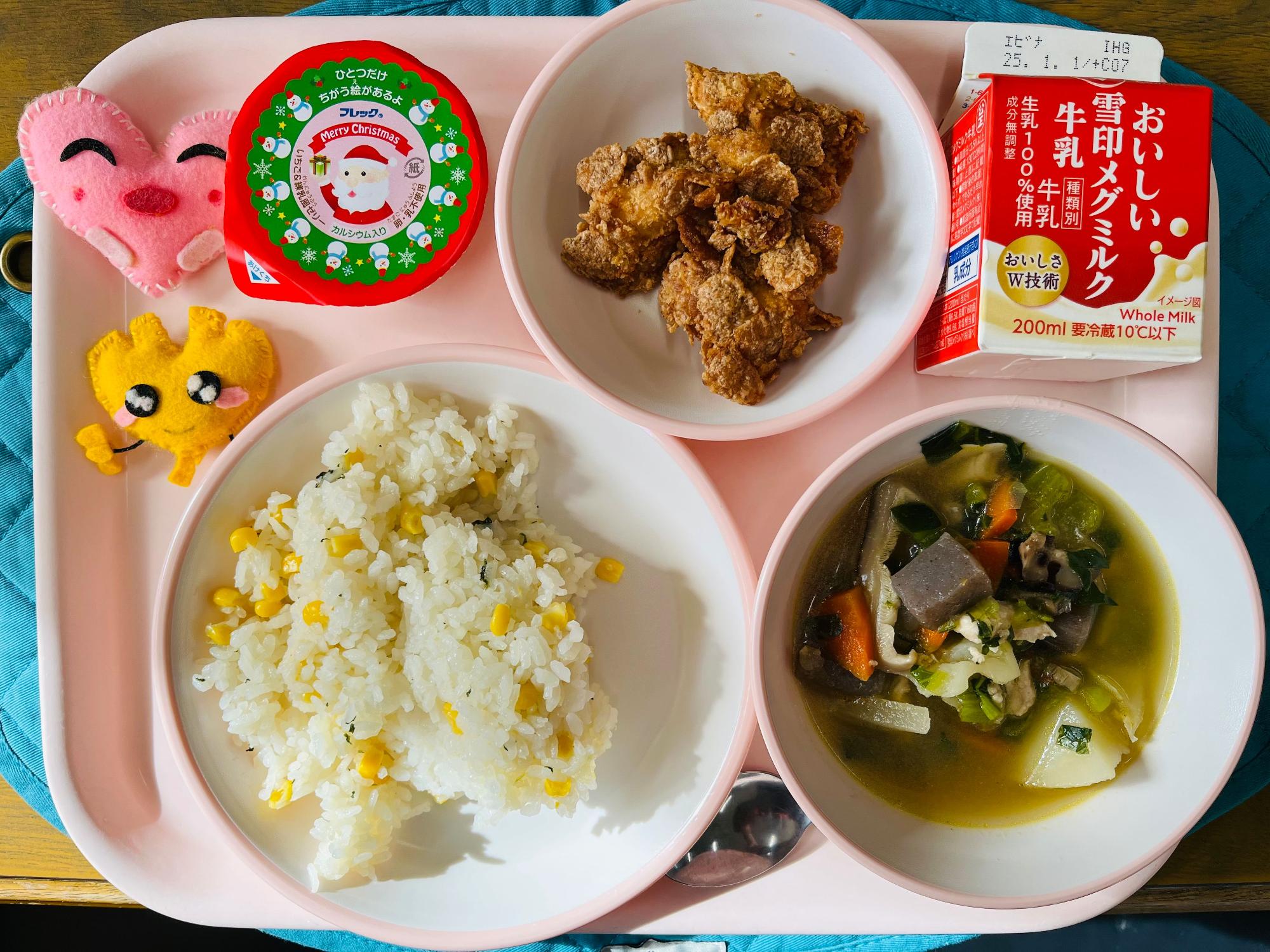 ピンクのトレーに給食が右上から反時計回りで牛乳、クリスピーチキン、クリスマスゼリー、ハートの形をした黄色とピンク色の布製マスコット、コーンピラフ、和風ポトフと並べられている写真