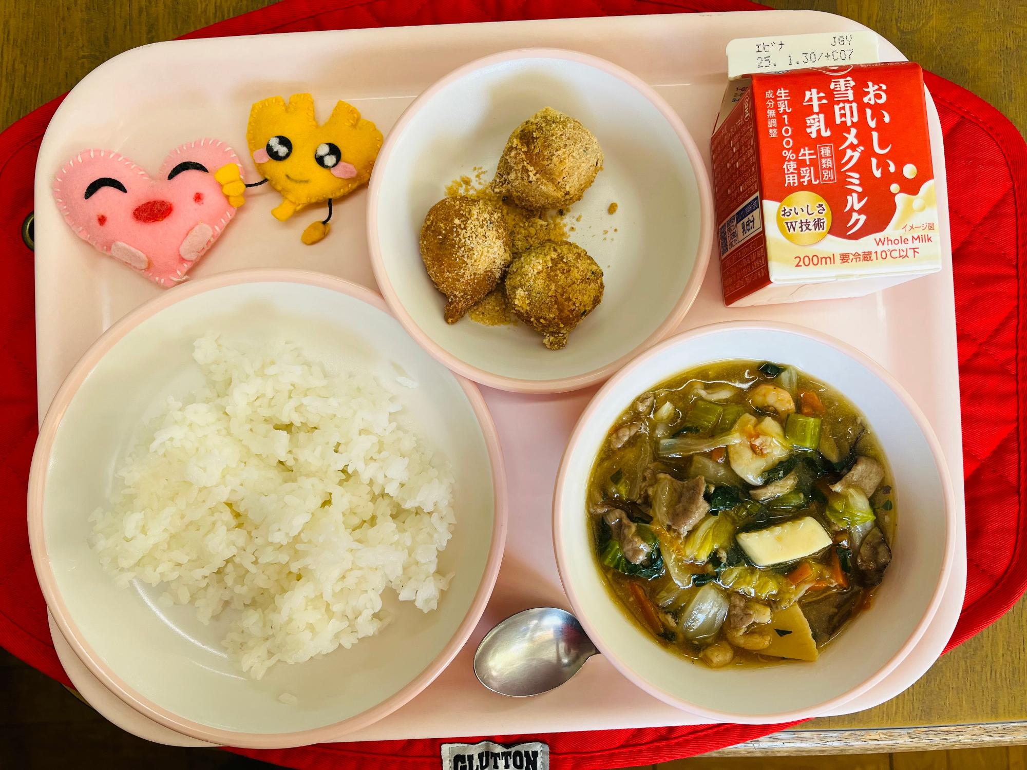 ピンクのトレーに給食が右上から反時計回りで牛乳、きなこドーナツ、ハートの形をした黄色とピンク色の布製マスコット、ごはん、中華丼の具と並べられている写真
