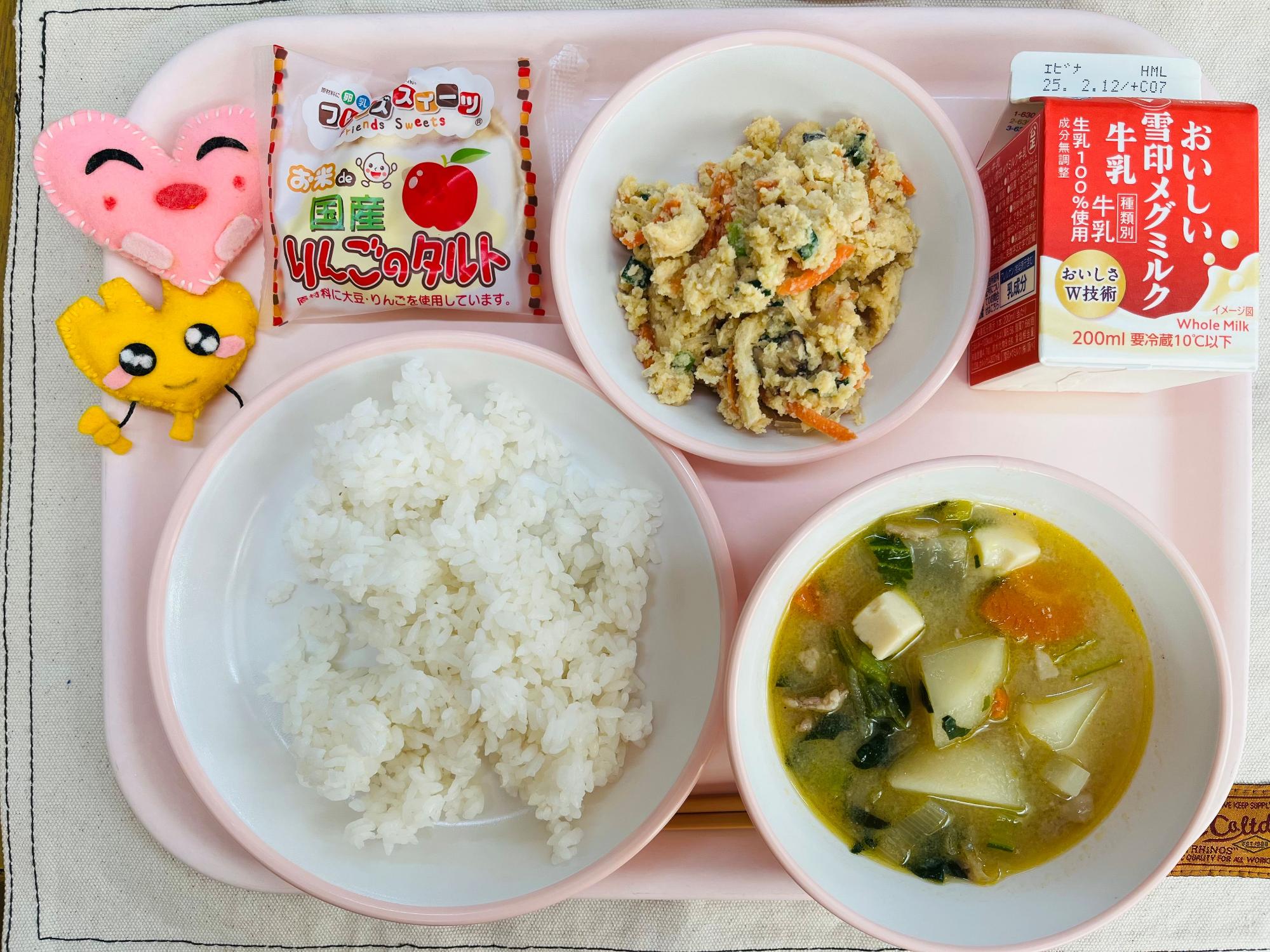 ピンクのトレーに給食が右上から反時計回りで牛乳、卯の花、りんごタルト、ハートの形をした黄色とピンク色の布製マスコット、ごはん、豚汁と並べられている写真