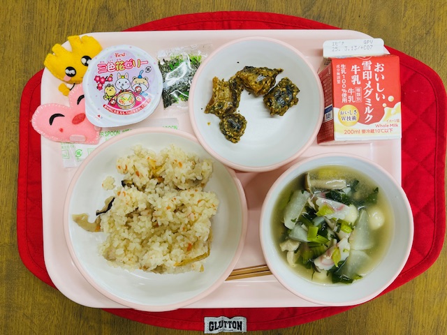 ピンクのトレーに給食が右上から反時計回りで牛乳、鯖のごま揚げ、刻み海苔、三色ゼリー、ハートの形をした黄色とピンク色の布製マスコット、ちらし寿司、白玉汁と並べられている写真