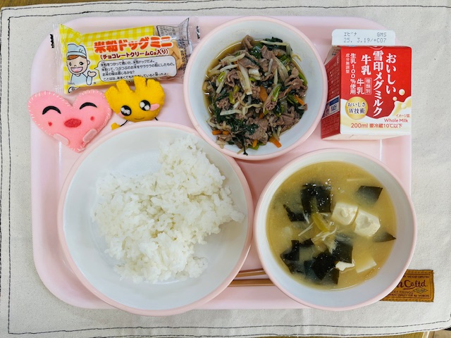 ピンクのトレーに給食が右上から反時計回りで牛乳、牛肉ビビンバ、米粉ドック、ハートの形をした黄色とピンク色の布製マスコット、ごはん、味噌汁と並べられている写真