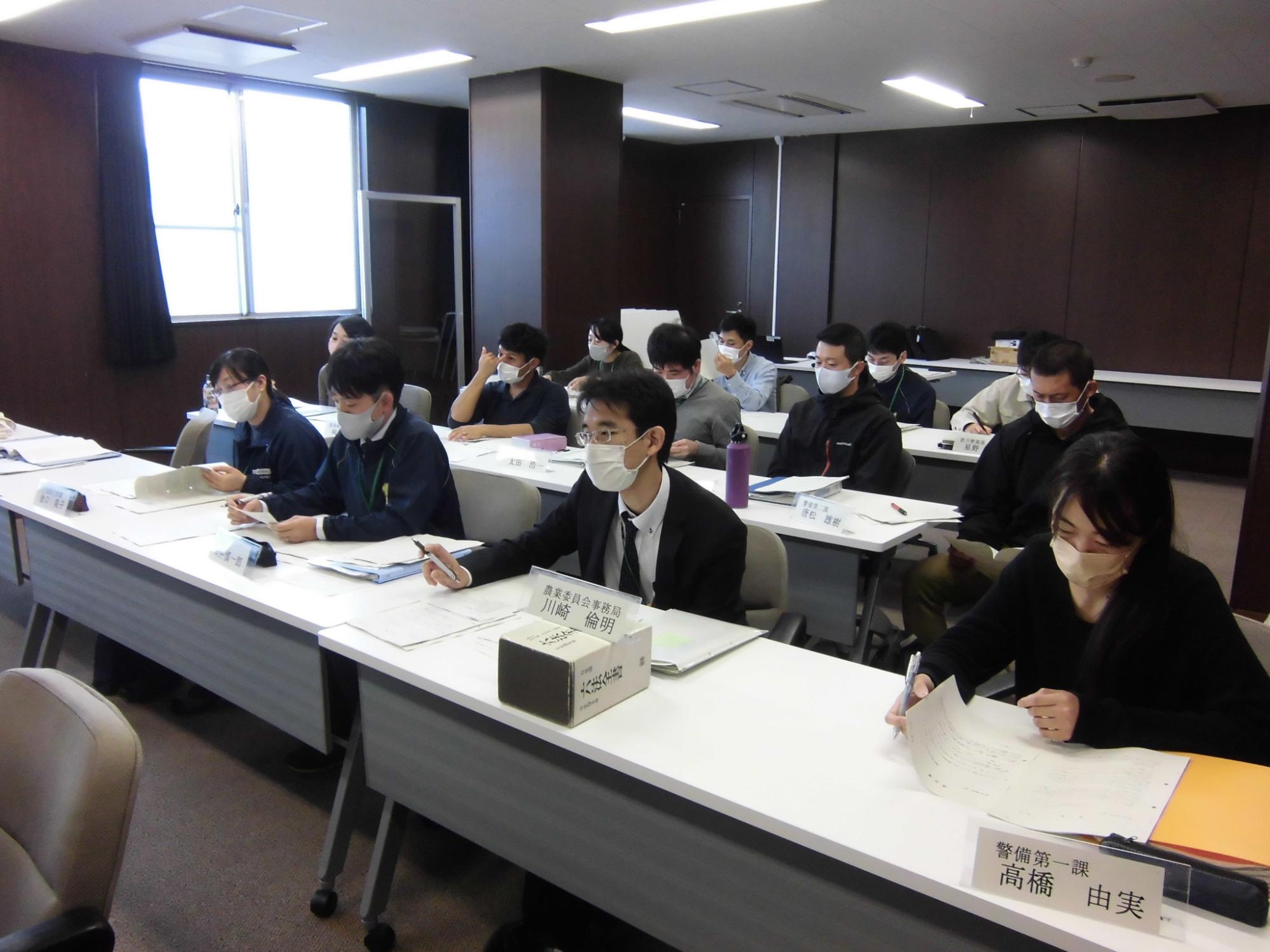 白い長テーブルが並んだ会議室で、大勢の参加者が、資料を広げて熱心に研修に参加している様子の写真