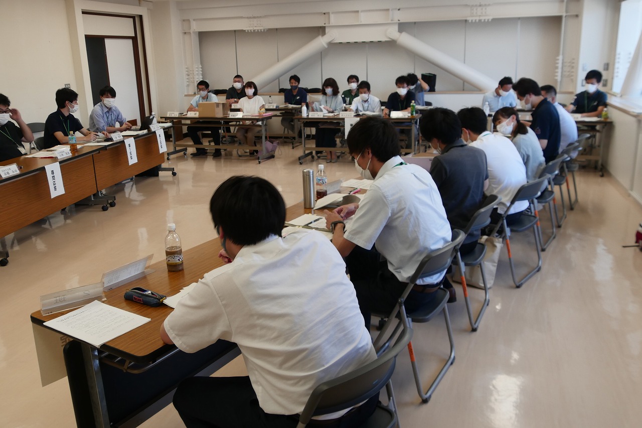 複数の机をコの字型に配置した会議室で、大勢の参加者資料を前に着席している研修の様子の写真