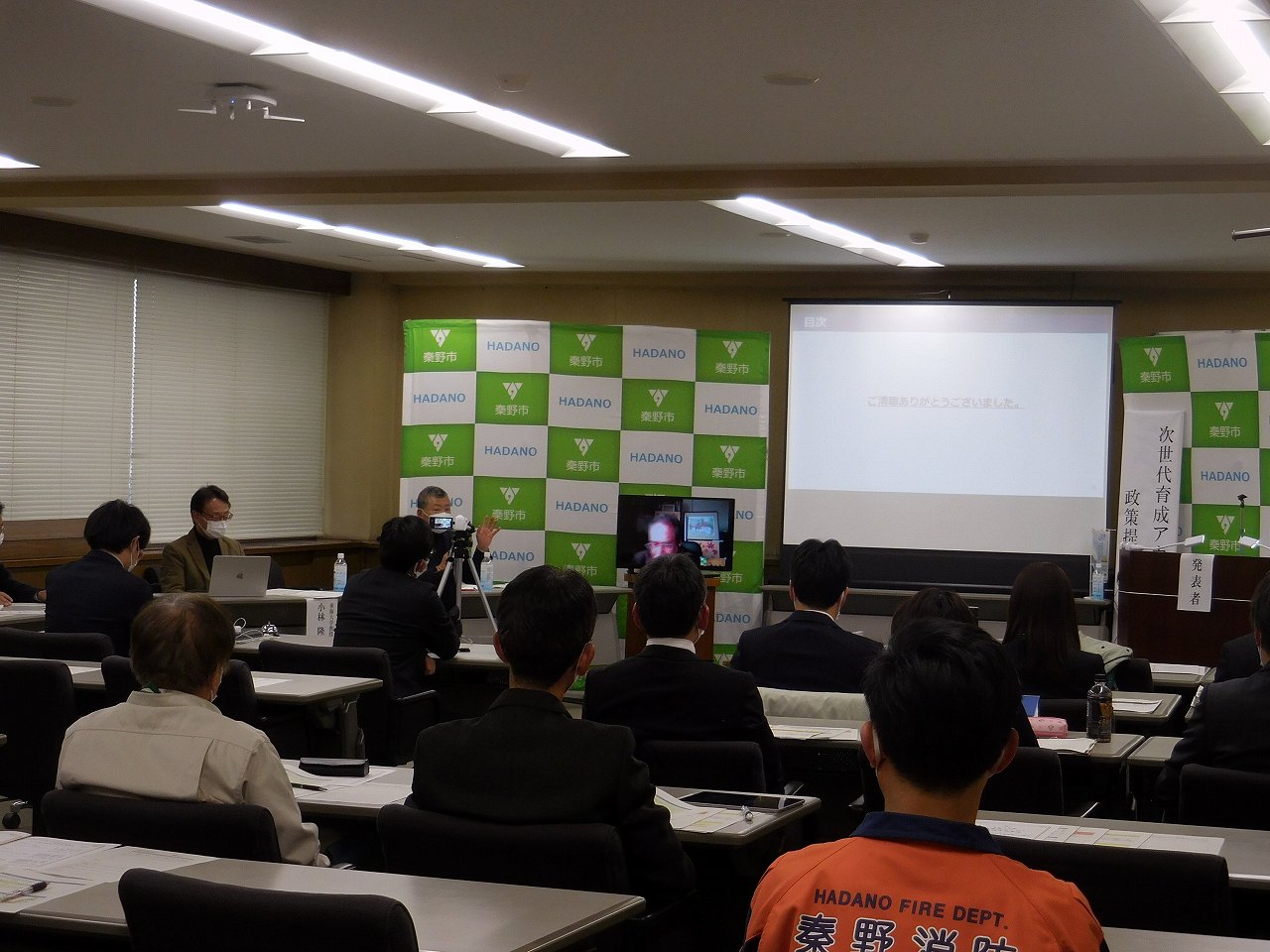 大勢の参加者が着席し、スクリーンに映る映像を視聴している「次世代育成アカデミー」政策提言発表会の様子の写真