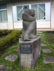 台座の上にお尻をつけ両膝を立て交差したポーズをした石像のモニュメント「陽光」写真